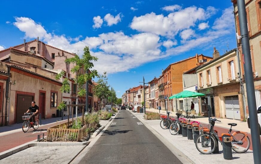 Sunny town street with buildings, parked bikes, and a cyclist.