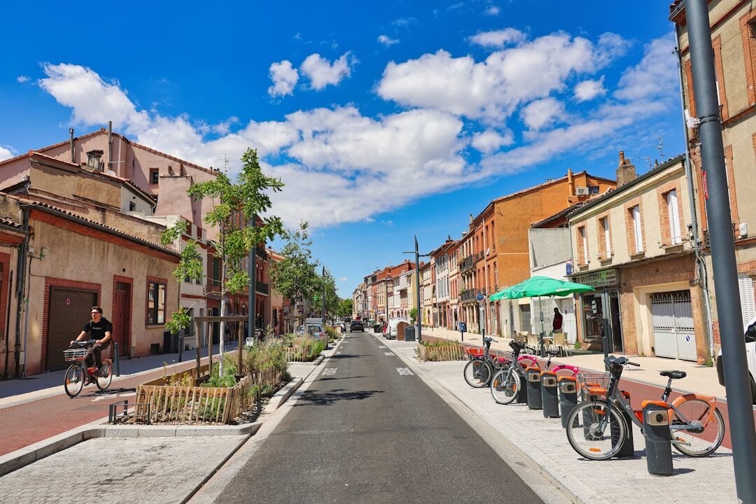 Sunny town street with buildings, parked bikes, and a cyclist.