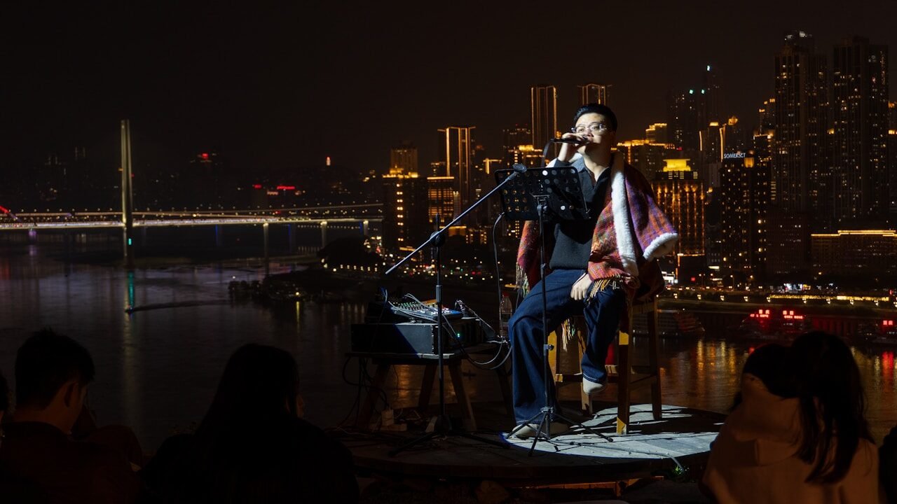 Man singing on stage with city lights behind