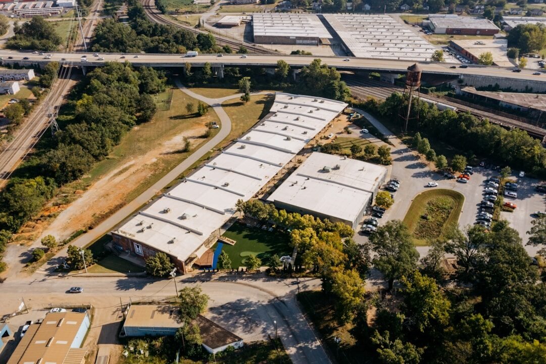 Aerial view of industrial buildings with surrounding trees and roads.