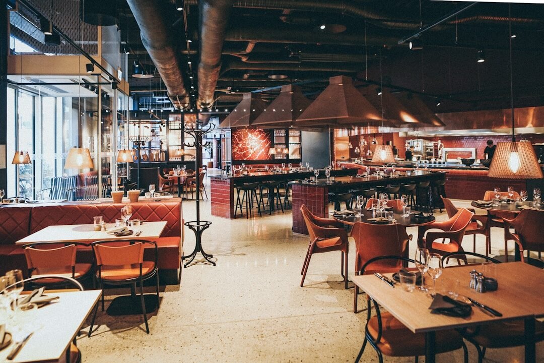 A modern restaurant interior with red leather booths, wooden tables, and hanging pendant lights
