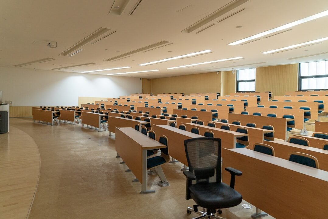Rows of wooden desks and chairs in a large empty university lecture hall