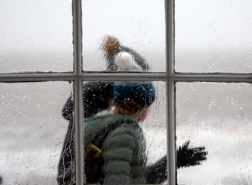 glass window across person wearing gray bubble jacket