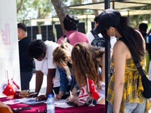 People signing papers at an outdoor table with flags