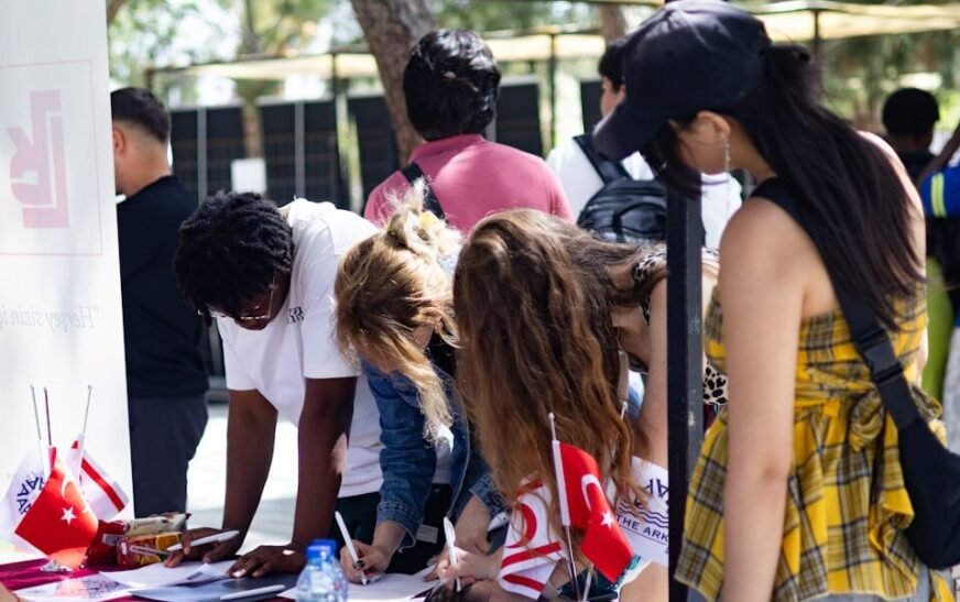 People signing papers at an outdoor table with flags