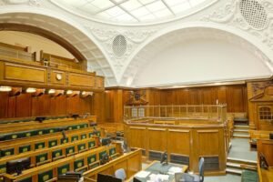 Empty ornate courtroom interior with wooden paneling and green seats.