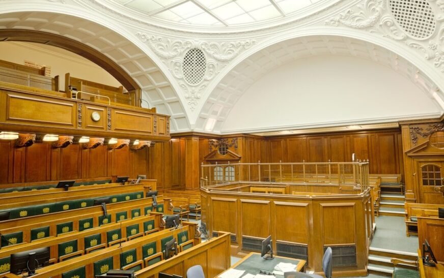 Empty ornate courtroom interior with wooden paneling and green seats.